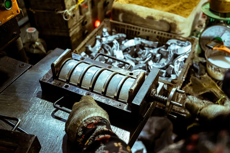 Close-up of a worker operating a metal bending machine in a workshop setting, highlighting industrial tools and materials.