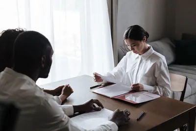 A professional woman reviews documents with a couple at home, indicating a collaborative decision-making process.