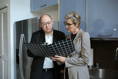 Two business professionals review documents in a modern office kitchen setting.